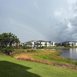 an apartment building with a pond and a rainbow in the sky